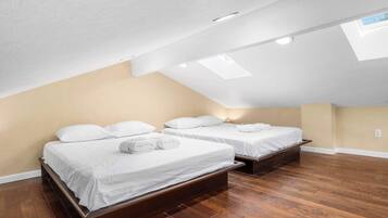 Una habitación con dos camas, suelo de madera y techo inclinado con tragaluces.