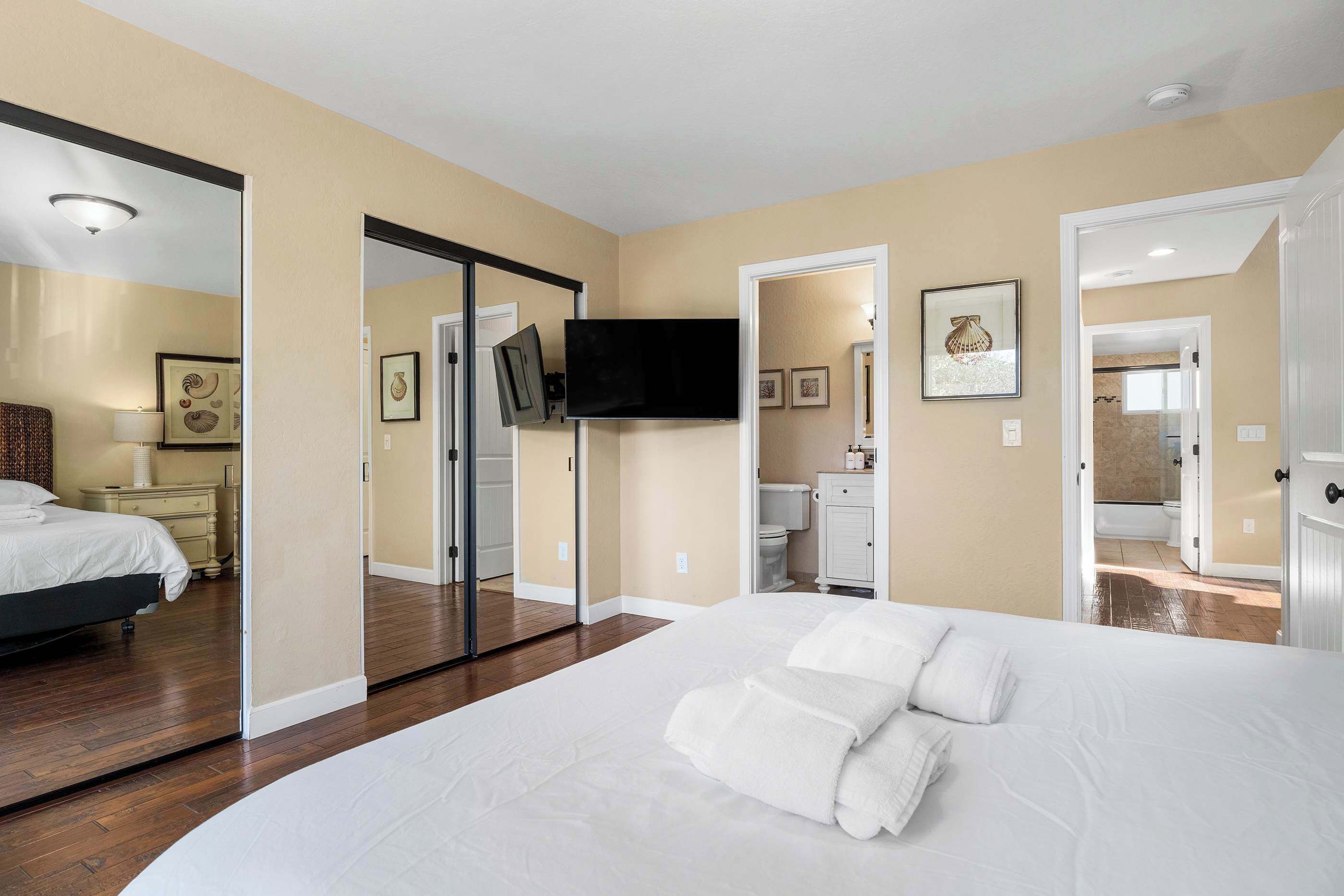 Une chambre d’hôtel avec un grand lit, un téléviseur à écran plat fixé au mur, une salle de bain visible à travers une porte ouverte et un miroir qui reflète la pièce.