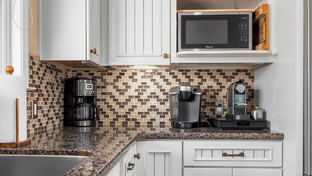 A kitchen with white cabinets, a microwave, a coffee maker, and a tiled backsplash. - Capitola Village Home - Free Parking & Sleeps 8! (Capitola)