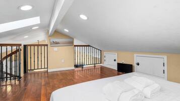 A spacious attic bedroom with a large bed, a TV, and a staircase leading to another level.