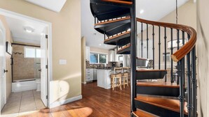 A modern kitchen with a central island, wooden flooring, and a spiral staircase with black railings. - Capitola Village Home - Free Parking & Sleeps 8! (Capitola)