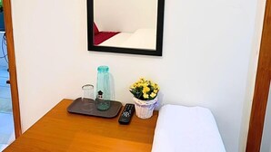 Un petit bureau en bois sur lequel on trouve un cadre avec une photo, une télécommande, une bouteille en verre et un panier rempli de fleurs jaunes.