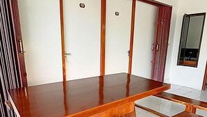 Une grande table à manger en bois, avec des bancs, dans une pièce dont le sol est recouvert de carreaux blancs et qui possède un plafond haut.