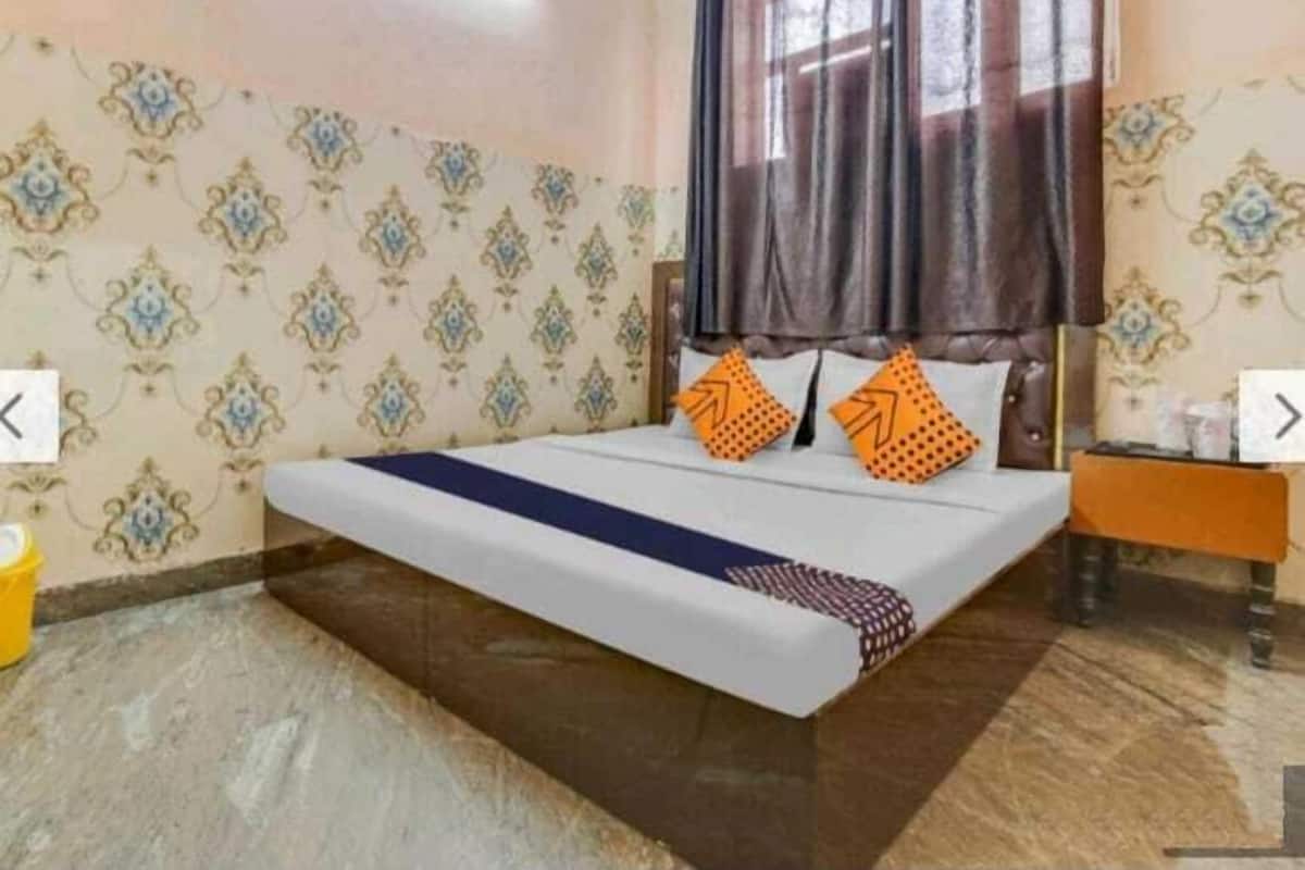 A bedroom with a bed, patterned wallpaper, a window with curtains, and a nightstand.