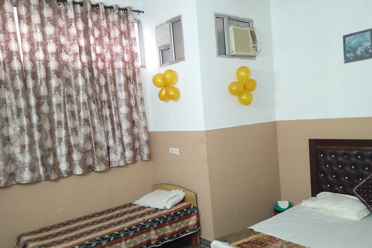 A bedroom with two beds, a window, an air conditioner, and yellow balloons on the wall.