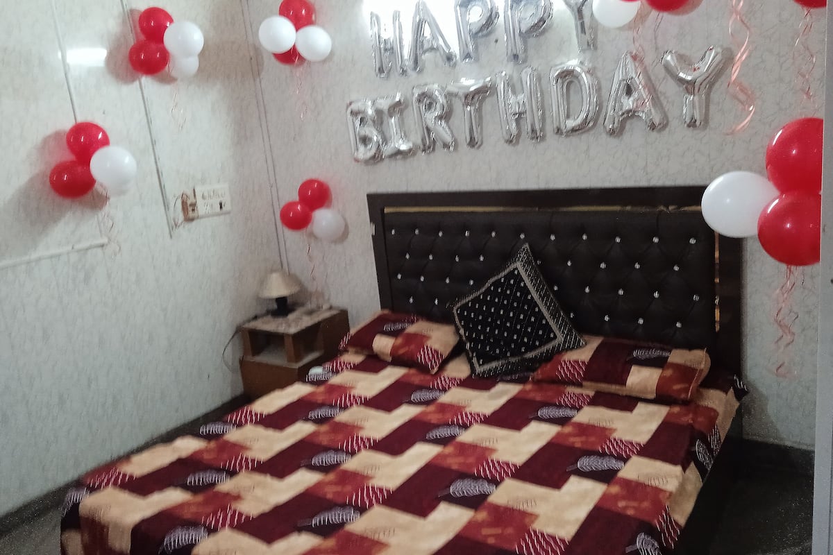 A bedroom with a bed, a nightstand, and a wall decorated with balloons and a 'Happy Birthday' sign.