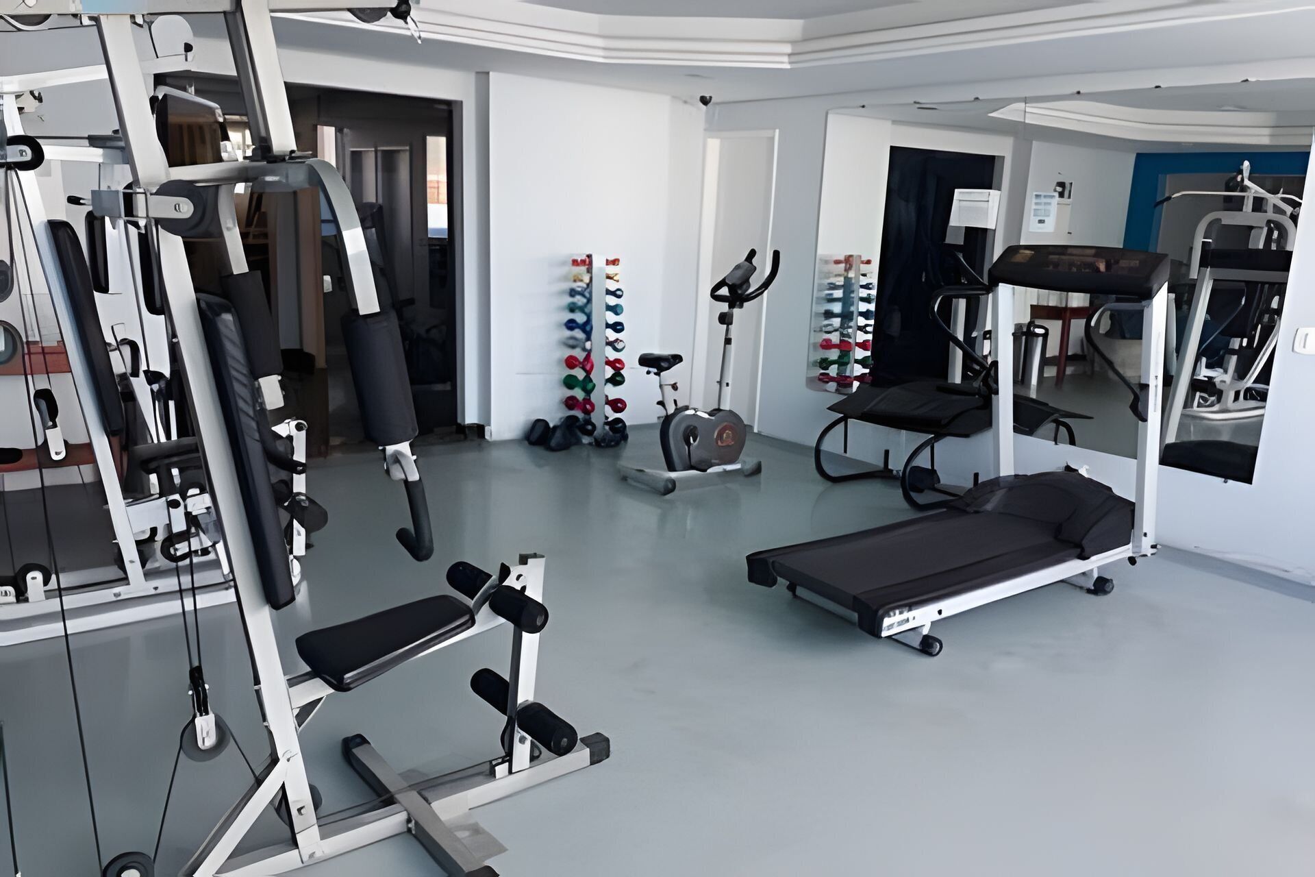Een sportschool met diverse fitnessapparaten, een bank en een spiegelwand.