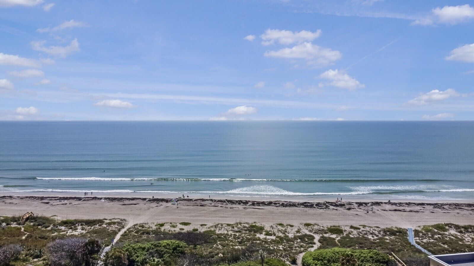 Ein Strand mit freiem Blick auf den Ozean, einem sandigen Ufer und etwas Vegetation im Vordergrund.