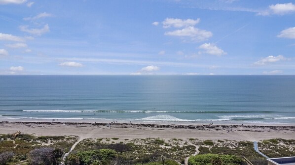 A beach with a clear view of the ocean, a sandy shore, and some vegetation in the foreground.