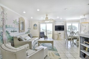 A living room with a sofa, armchairs, a coffee table, a TV, and a balcony with a view.