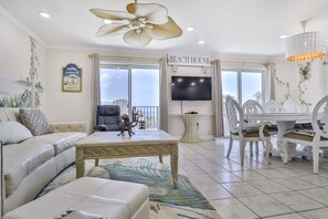 A living room with a sofa, a coffee table, a TV, a dining table with chairs, and a ceiling fan.