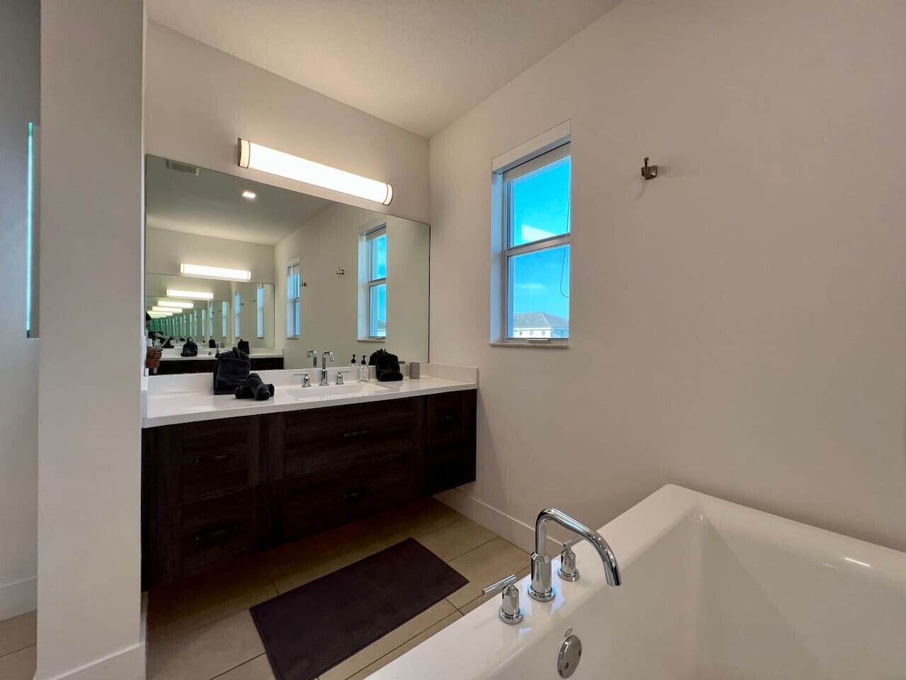 Un baño moderno con un espejo grande, dos lavamanos, una bañera y una ventana.