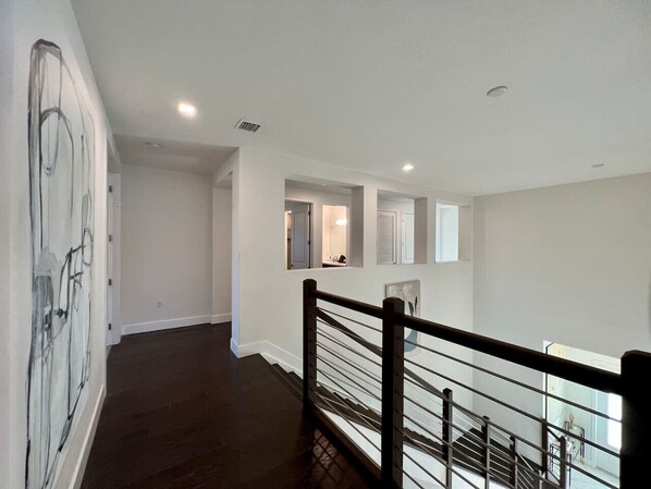 A spacious, well-lit hallway with a dark wooden floor, white walls, and a black railing.