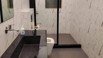 A modern bathroom with a marble wall, a black sink, a toilet, and a mirror.