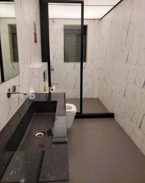 A modern bathroom with a marble wall, a black sink, a toilet, and a mirror.