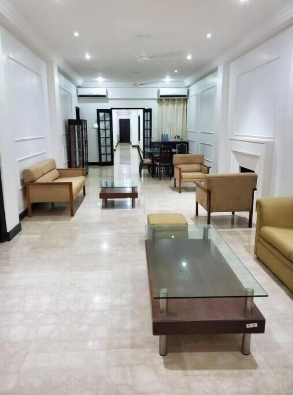 A spacious living room with a glass coffee table, beige sofas, and a dining area in the background.