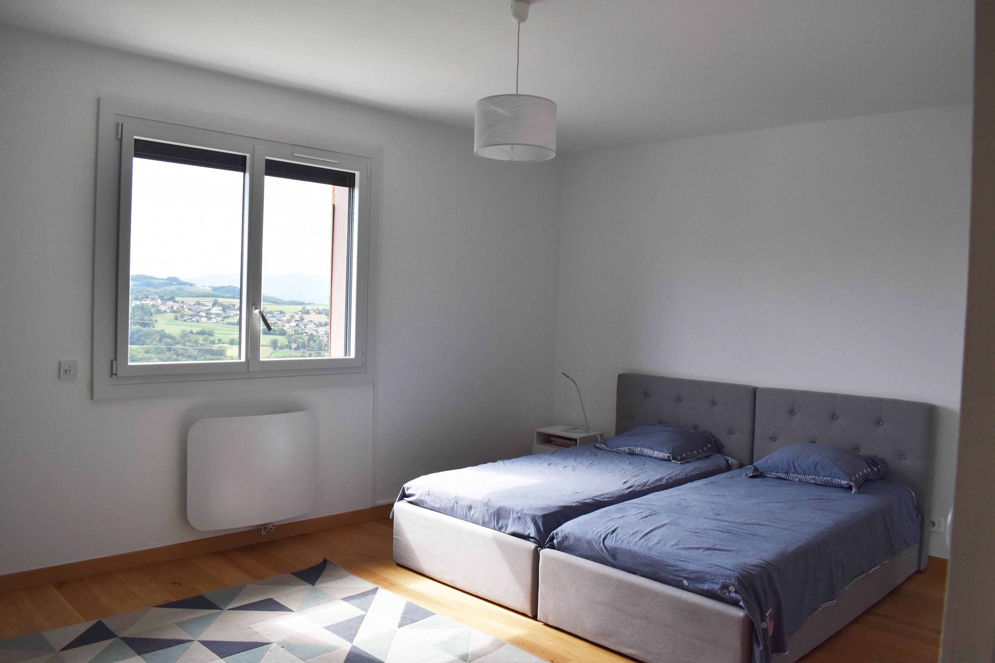 Un dormitorio con un ventanal grande, una cama, una mesita de noche y una lámpara de pie.