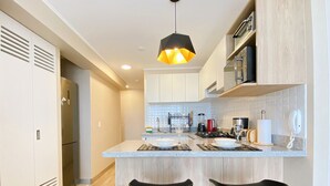 A modern kitchen with a central island, bar stools, a hanging light fixture, and a built-in oven. - R Lindo departamento 1BR en Miraflores (Lima)