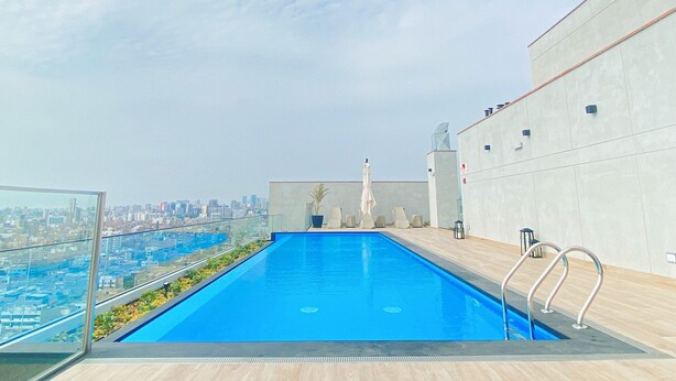 A rooftop pool with a city view, surrounded by a modern building with a concrete exterior. - R Lindo departamento 1BR en Miraflores (Lima)