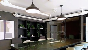 A modern conference room with a glass table, multiple chairs, pendant lighting, and a plant wall. - R Lindo departamento 1BR en Miraflores (Lima)