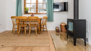 Une pièce chaleureuse avec une table et des chaises en bois, un téléviseur fixé au mur et un poêle à bois noir.