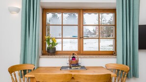 Une table de salle à manger en bois, accompagnée de quatre chaises, une fenêtre aux vitres dépolies et une vue sur un paysage enneigé.