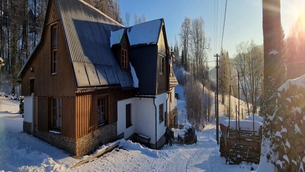 Une maison en bois avec un toit en pente, entourée d’un paysage enneigé et d’arbres.
