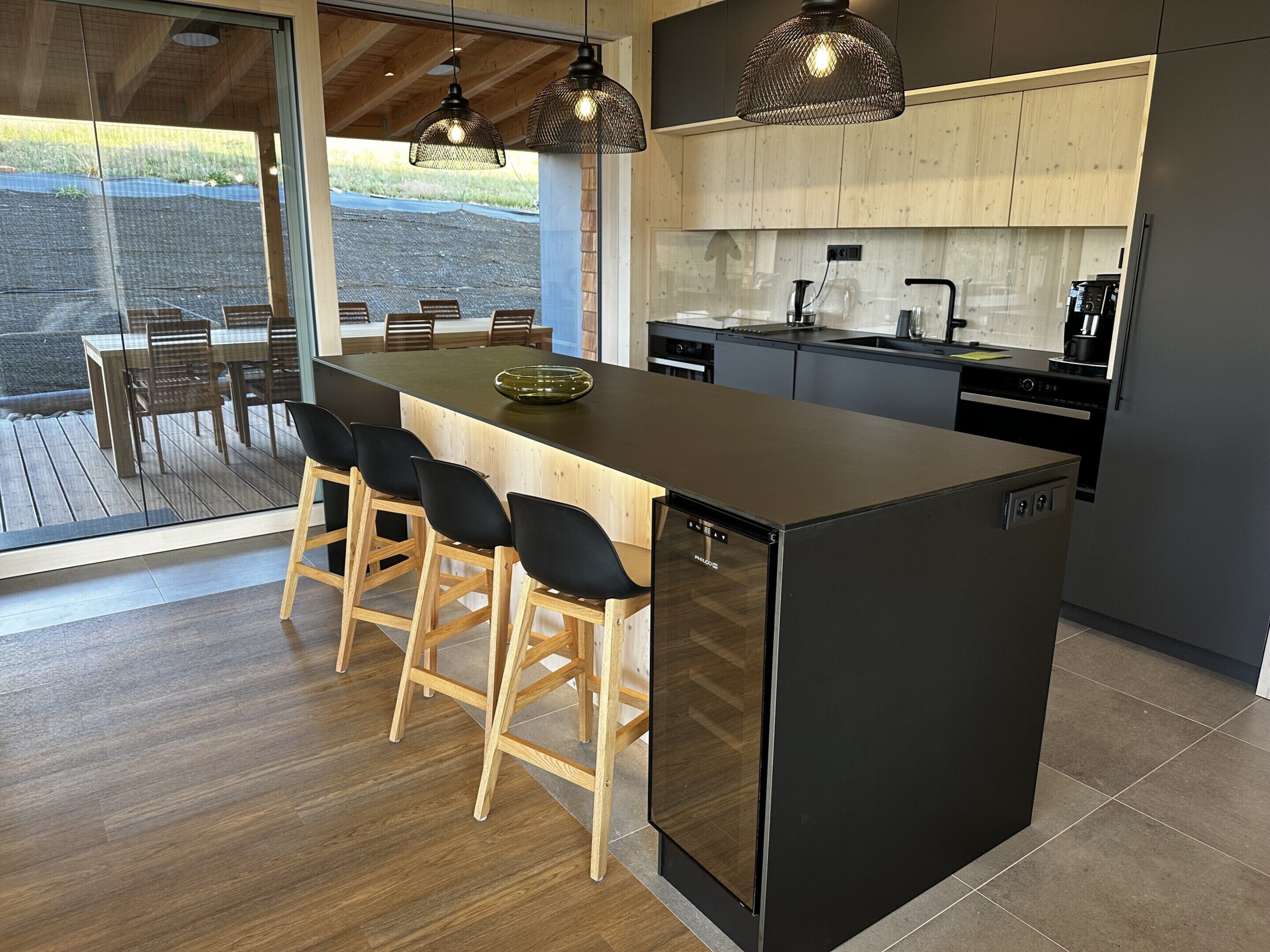 Een moderne keuken met een centraal eiland, barstoelen en een uitzicht door grote ramen.