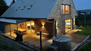 A modern house with a sloped roof, large windows, and a wooden deck. - Holiday Home in Roprachtice With Sauna & Jacuzzi (Roprachtice)