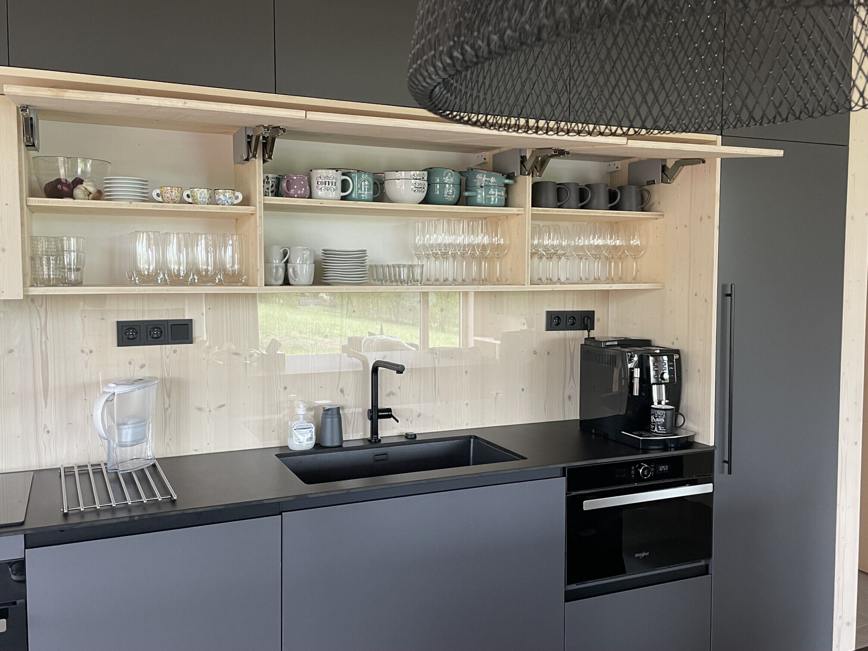 Una cocina moderna con estantes abiertos que exhiben cristalería y tazas, una cafetera y un horno empotrado.