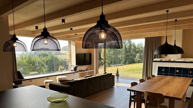 A modern kitchen with a large island, wooden dining table, and hanging pendant lights. - Holiday Home in Roprachtice With Sauna & Jacuzzi (Roprachtice)