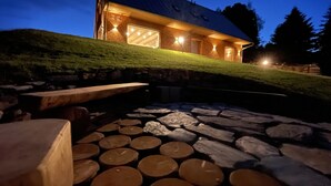 A stone patio with logs, a wooden bench, and a building with a garage. - Holiday Home in Roprachtice With Sauna & Jacuzzi (Roprachtice)