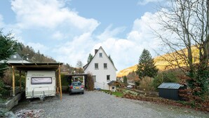 A gravel driveway leading to a white house with a covered porch and a parked camper. - Appartementen Am Forstweg Yalet (Brilon)