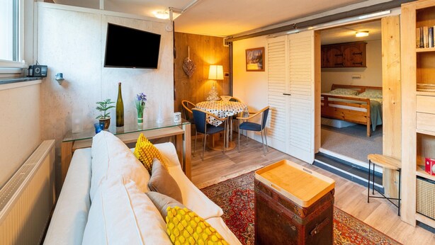 A cozy living room with a sofa, a dining table, and a TV mounted on the wall. - Appartementen Am Forstweg Yalet (Brilon)