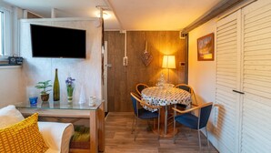 A compact living space with a dining area, a television mounted on the wall, and a small table with chairs. - Appartementen Am Forstweg Yalet (Brilon)