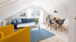 A cozy loft-style room with a high ceiling, a blue sofa, a yellow armchair, a dining table with chairs, and a large window providing natural light. - 5 Star Holiday Home in Hjorring (Hjørring)