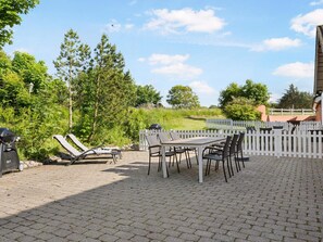 An outdoor patio with a table and chairs, surrounded by a white picket fence, and a grill in the foreground. - 5 Star Holiday Home in Hjorring (Hjørring)