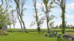 A grassy outdoor area with picnic tables and benches, surrounded by trees and a clear sky. - 5 Star Holiday Home in Hjorring (Hjørring)