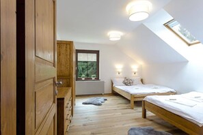 Een knus slaapkamer met twee eenpersoonsbedden, een houten garderobe, een dakraam en een raam met uitzicht op groen.