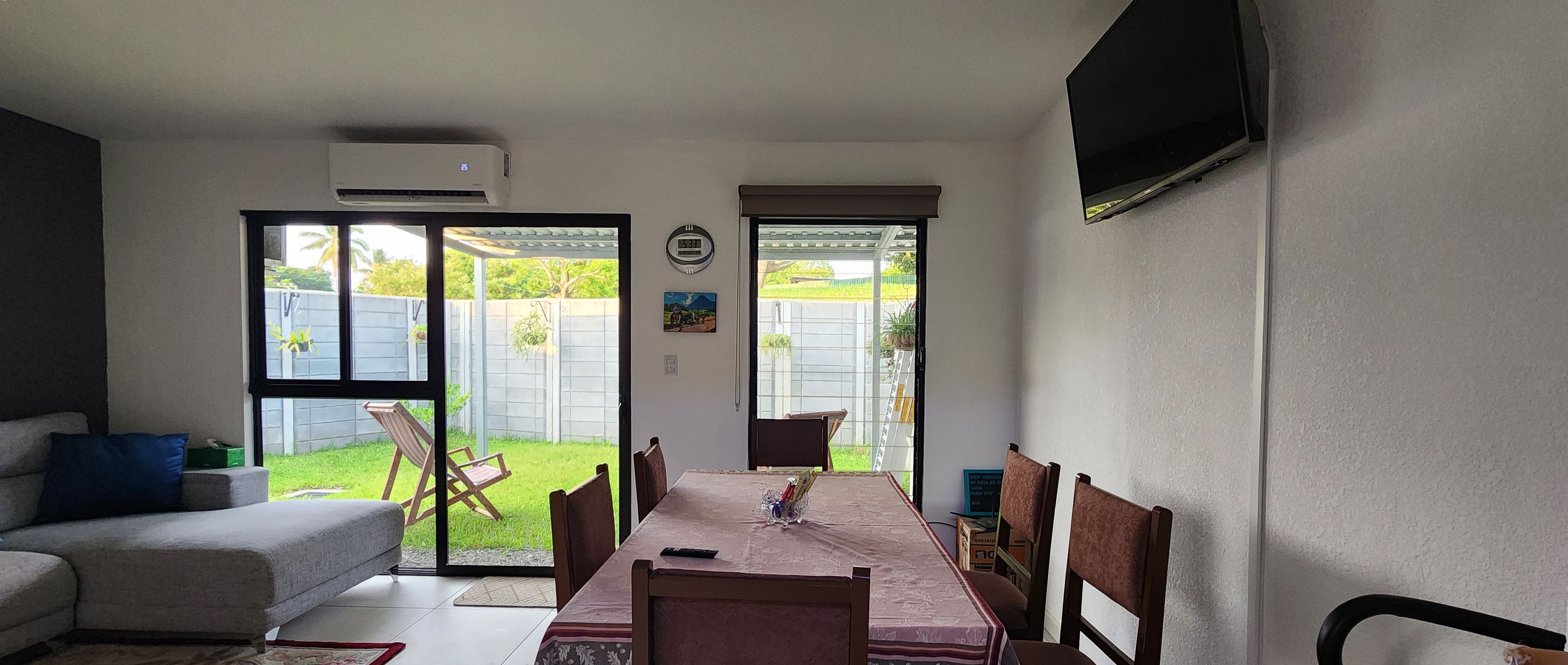 Un comedor con una mesa preparada para cuatro, un sofá y un televisor montado en la pared.