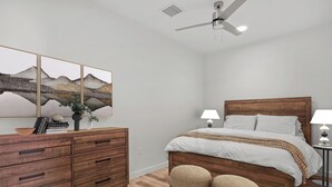 Ein Schlafzimmer mit einem hölzernen Bett, zwei Nachttischlampen, einem Deckenventilator, einer Kommode mit Schubladen und einem an der Wand befestigten Kunstwerk.