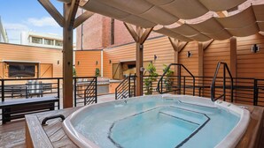 Ein Whirlpool auf einer Holzterrasse mit einer Pergola darüber, umgeben von Ziegelgebäuden.