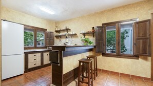 Eine Küche mit Kühlschrank, Schränken, einer Arbeitsplatte, Hockern und einem Fenster.