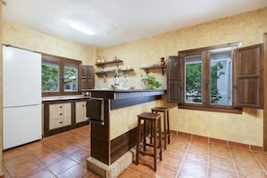Una cocina con refrigerador, armarios, encimera, taburetes y una ventana.