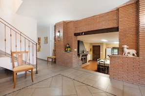 A living room with a brick fireplace, a wooden staircase, and a dining area.