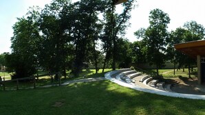 Un parque con un escenario y zona de asientos, rodeado de árboles y césped.