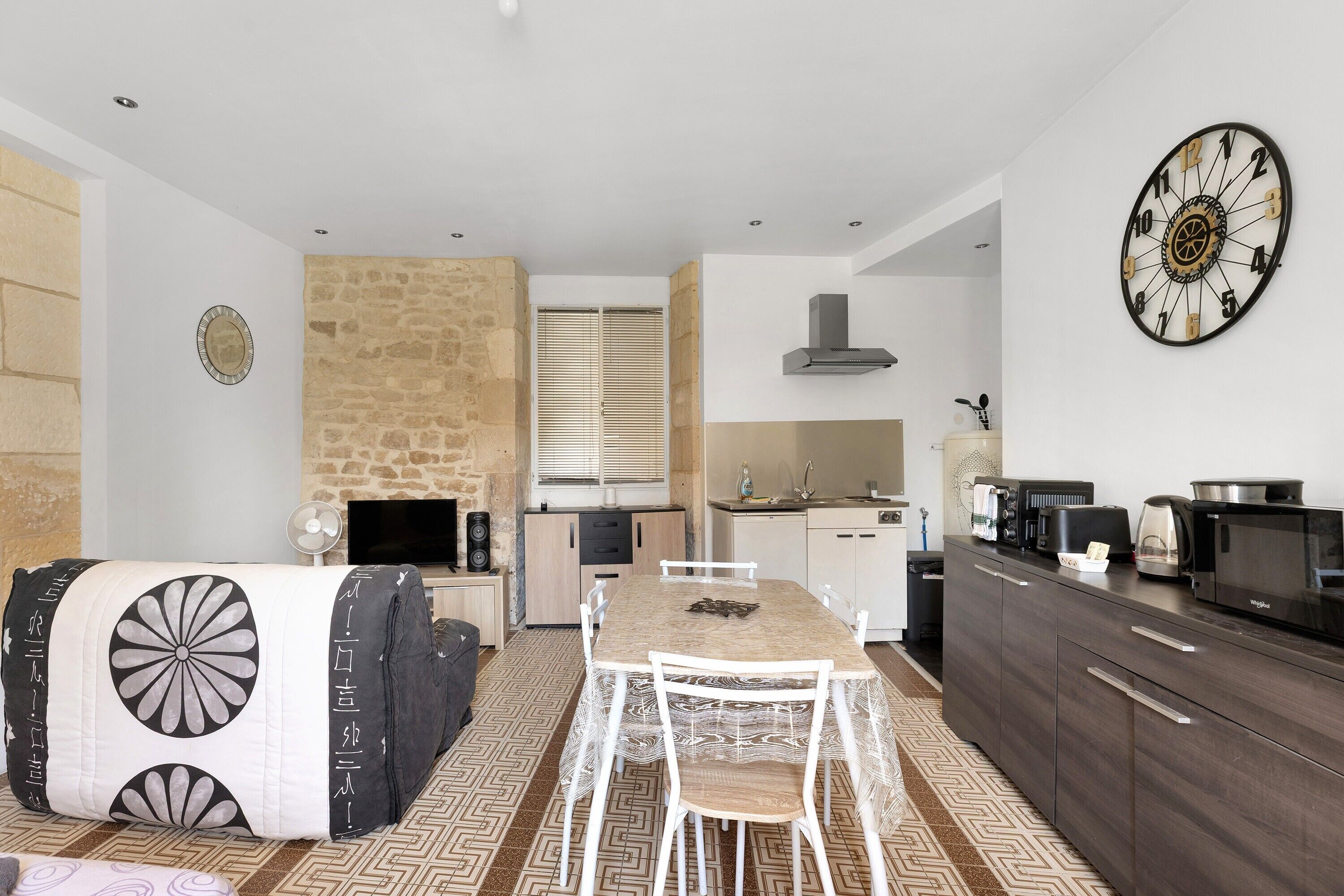 Une cuisine moderne avec une table à manger, des chaises blanches, un mur en pierre et une grande horloge.