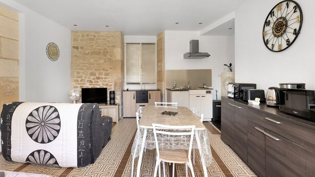 Una cocina moderna con una mesa de comedor, sillas blancas, una pared de piedra y un reloj grande.