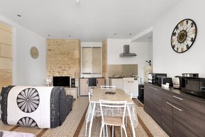 A modern kitchen with a dining table, white chairs, a stone wall, and a large clock.