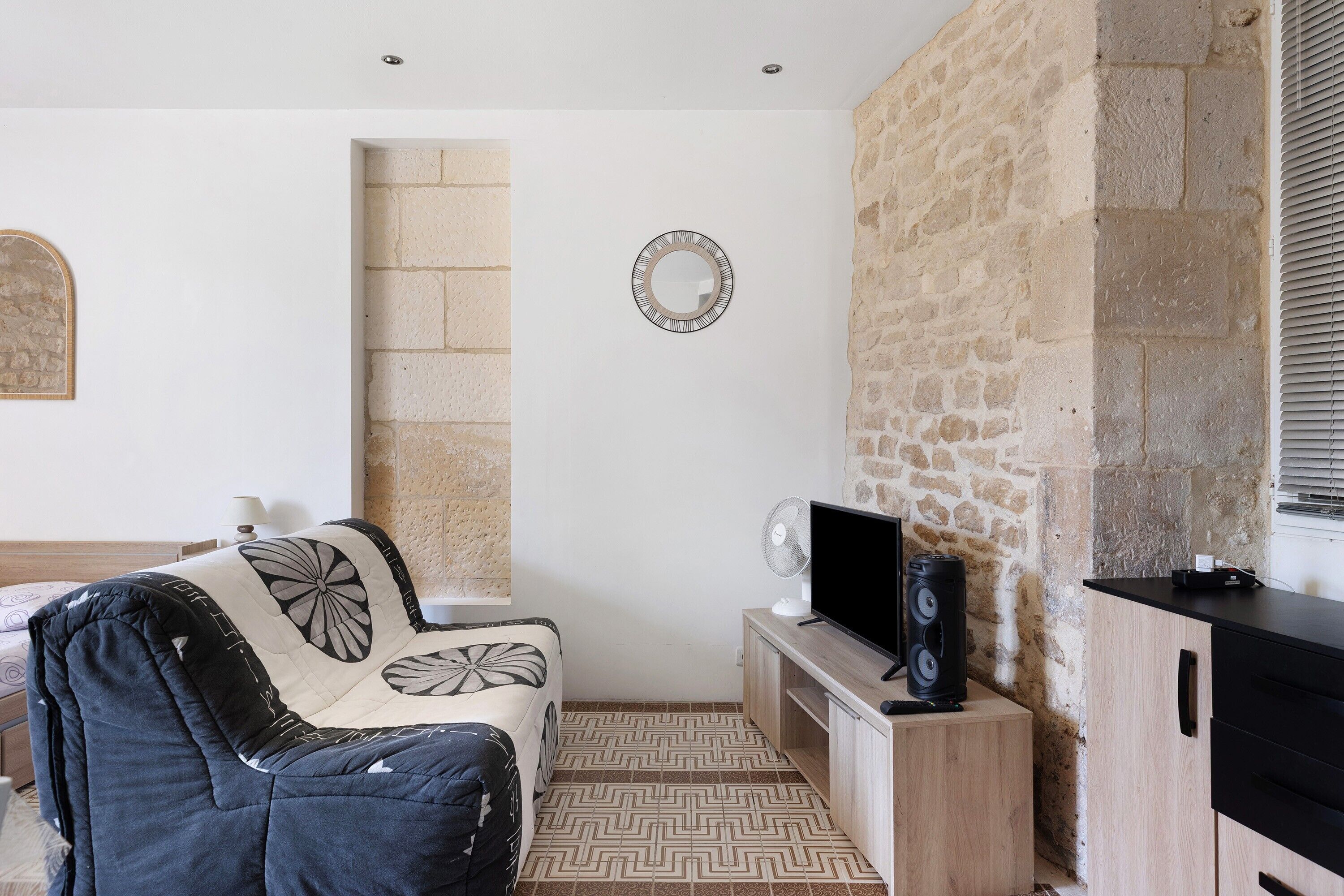 Une pièce avec un lit, une télévision, un haut-parleur, un miroir et un mur en pierre.